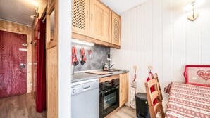 A compact kitchen with wooden cabinets, a dishwasher, an oven, and a small dining area with a red and white checkered tablecloth. - Apartment 'Les Pralyssimes 462' with Mountain View, Private Terrace and Wi-Fi (Taninges)