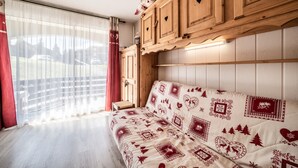 A room with a wooden cabinet, a patterned sofa, and a window with curtains. - Apartment 'Les Pralyssimes 462' with Mountain View, Private Terrace and Wi-Fi (Taninges)