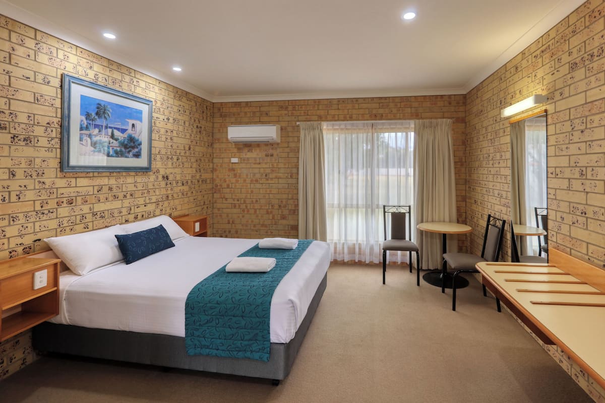 Habitación de hotel con cama, escritorio, silla, ventana con cortinas, equipo de aire acondicionado y televisor montado en la pared.