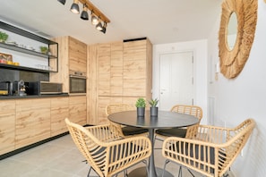 Een moderne keuken met houten kasten, een eettafel met rieten stoelen en een ronde spiegel aan de muur.