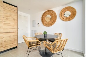 A dining area with a round table, wicker chairs, and two wall-mounted mirrors.
