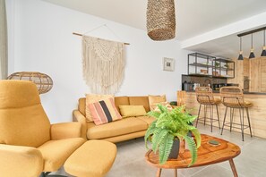 Een moderne woonkamer met een bank, fauteuil en een ronde houten salontafel met een plant erop.