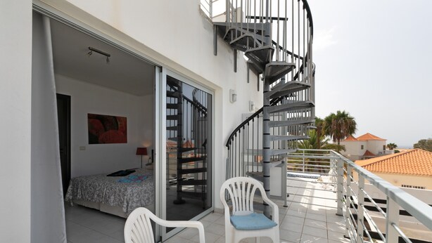 Ein Balkon mit einem Bett, einem Sessel, einem Tisch und einer Wendeltreppe.
