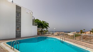 Ein Schwimmbecken mit Metallleiter, ein weißes Gebäude mit Naturstein-Fassade und Blick auf das Meer.