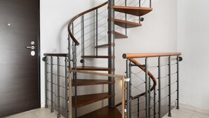 Eine Wendeltreppe mit Holzboden und Metallgeländern, die zu einer Zwischenebene mit einem Maschendraht-Geländer führt.