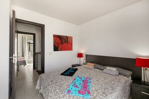 Une chambre d’hôtel avec un lit, une table de chevet, une lampe rouge, un tableau au mur et une porte donnant sur une autre pièce.