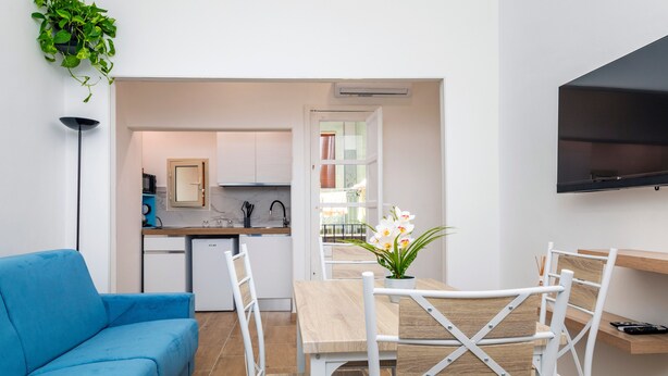 Un espace de vie moderne comprenant un canapé, une table à manger, des chaises, un coin cuisine et un téléviseur fixé au mur.