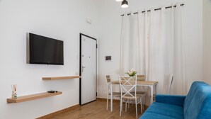 Un salon moderne avec un téléviseur à écran plat, un canapé bleu, une table à manger avec des chaises et un rideau blanc.