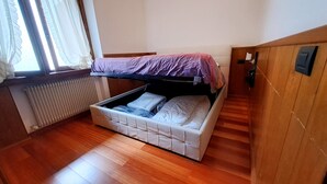 Une petite pièce avec un lit superposé, un radiateur, un plancher en bois et une fenêtre avec des rideaux.