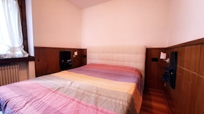 Un lit simple avec une couette, une tête de lit en bois et une fenêtre avec des rideaux.