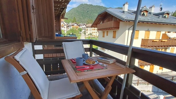 Un balcon avec une table dressée pour deux personnes, une chaise et une vue sur les bâtiments et les montagnes.