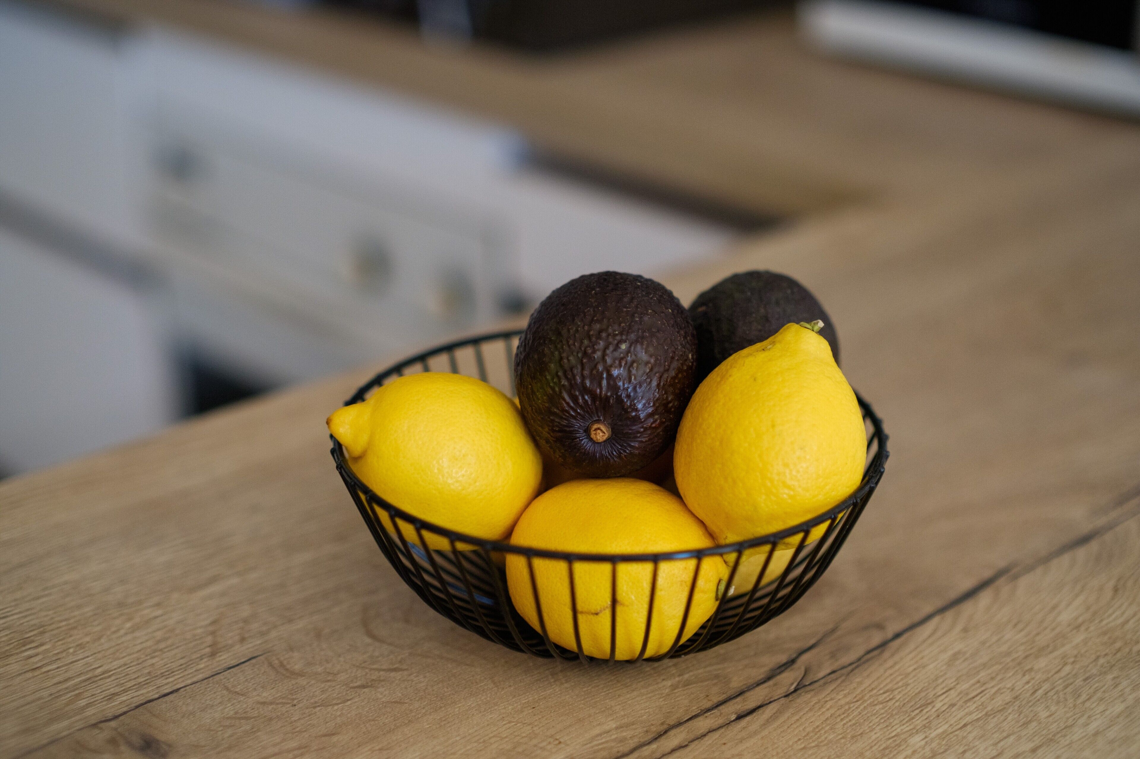 Ein Korbmöbel mit Zitronen und Avocados auf einer Holztischplatte.