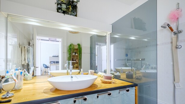 Ein modernes Badezimmer mit einem großen Spiegel, einem weißen Waschbecken und einer Duschkabine aus Glas.