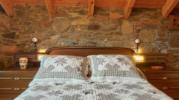 Ein Bett mit gemusterten Betttextilien, einem Holzkopfende, einer Steinwand und Nachttischlampen.