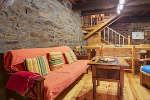 Ein gemütliches Zimmer mit Stehwänden, Holzmöbeln, einer Couch mit bunten Kissen, einem Holztisch und einer Treppe.