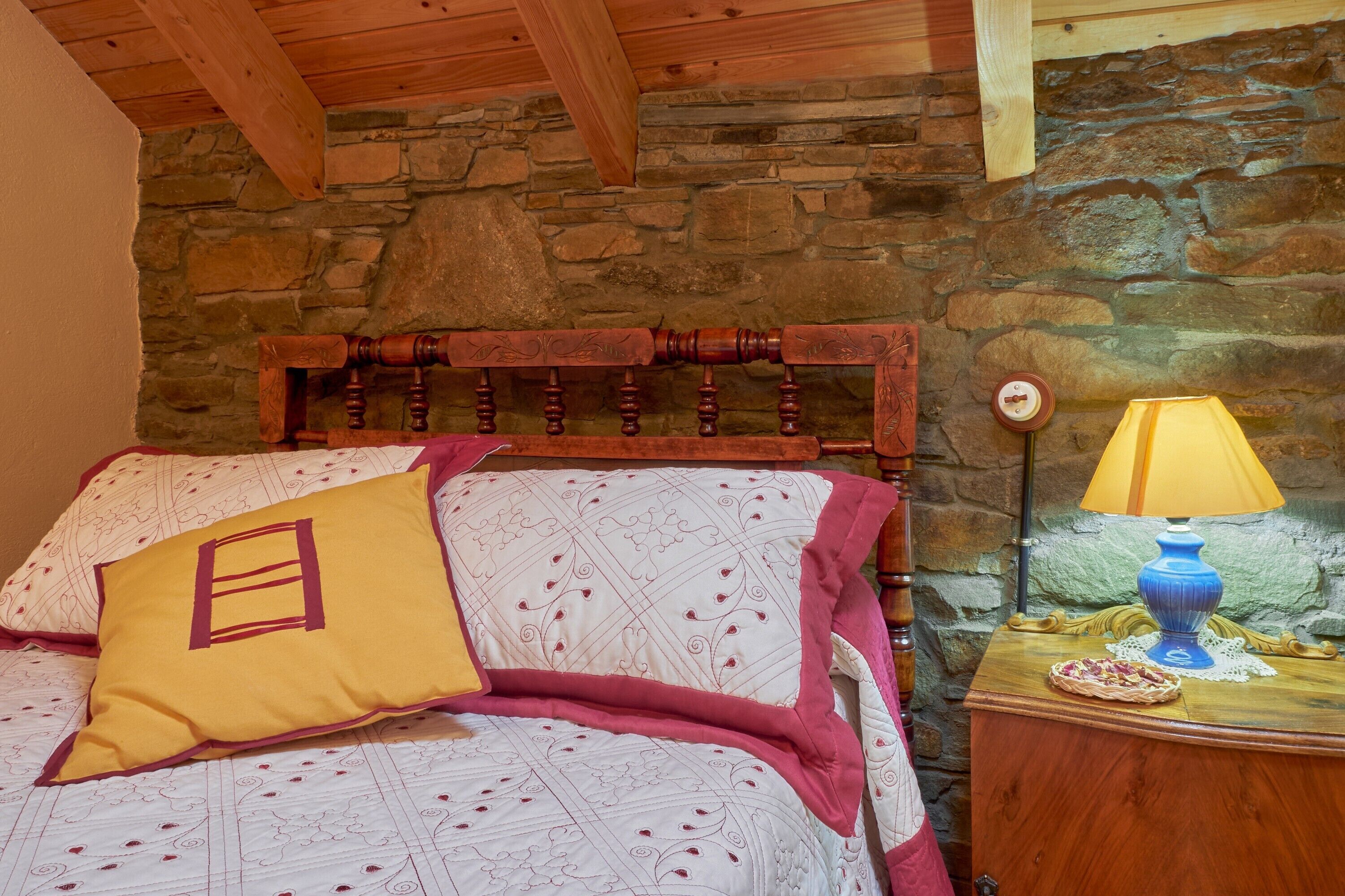 A bed with a wooden headboard, a yellow pillow, and a patterned bedspread.