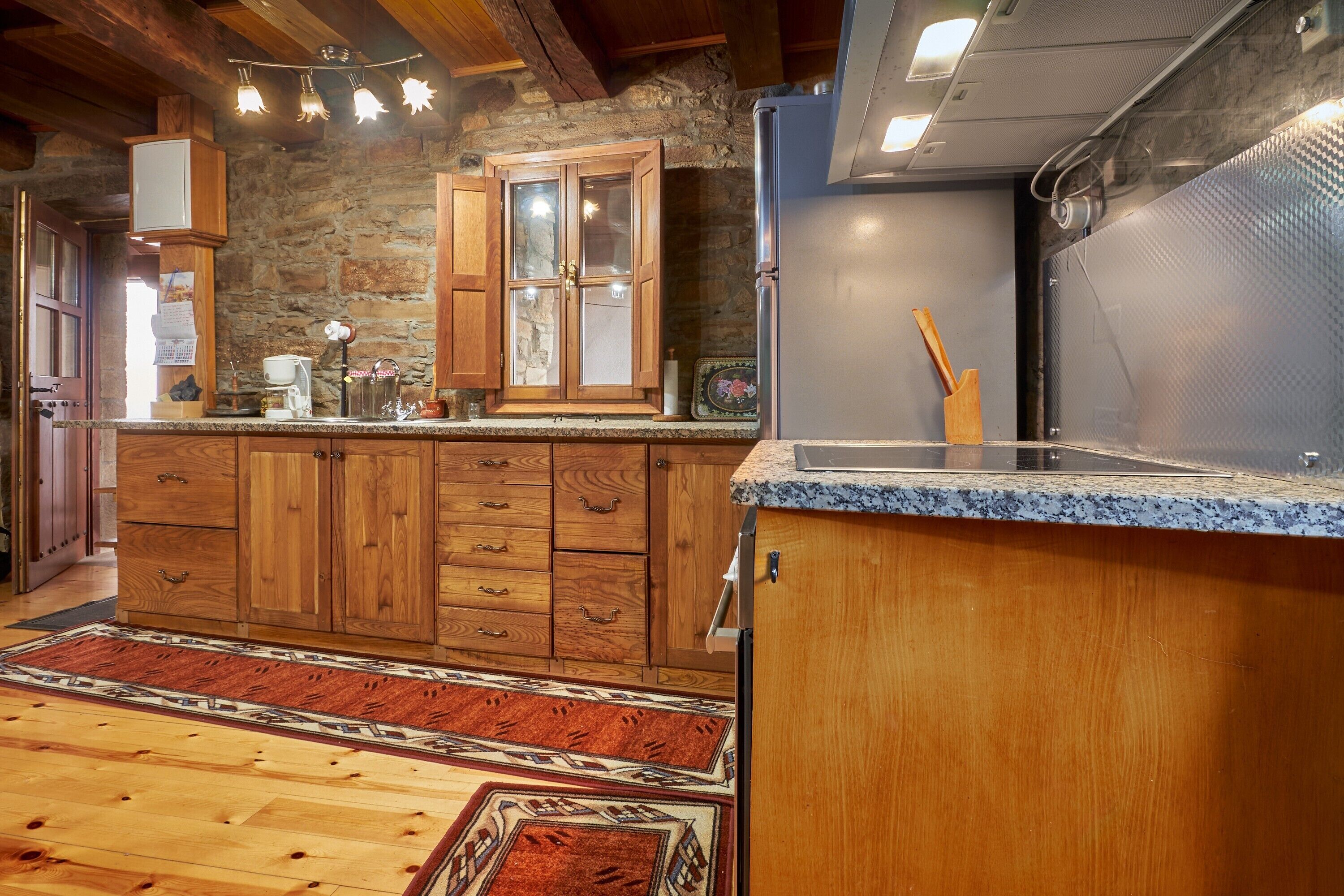 A kitchen with wooden cabinets, a granite countertop, and a stone wall.