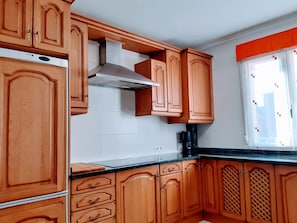 A kitchen with wooden cabinets, a stainless steel range hood, and a window with blinds.