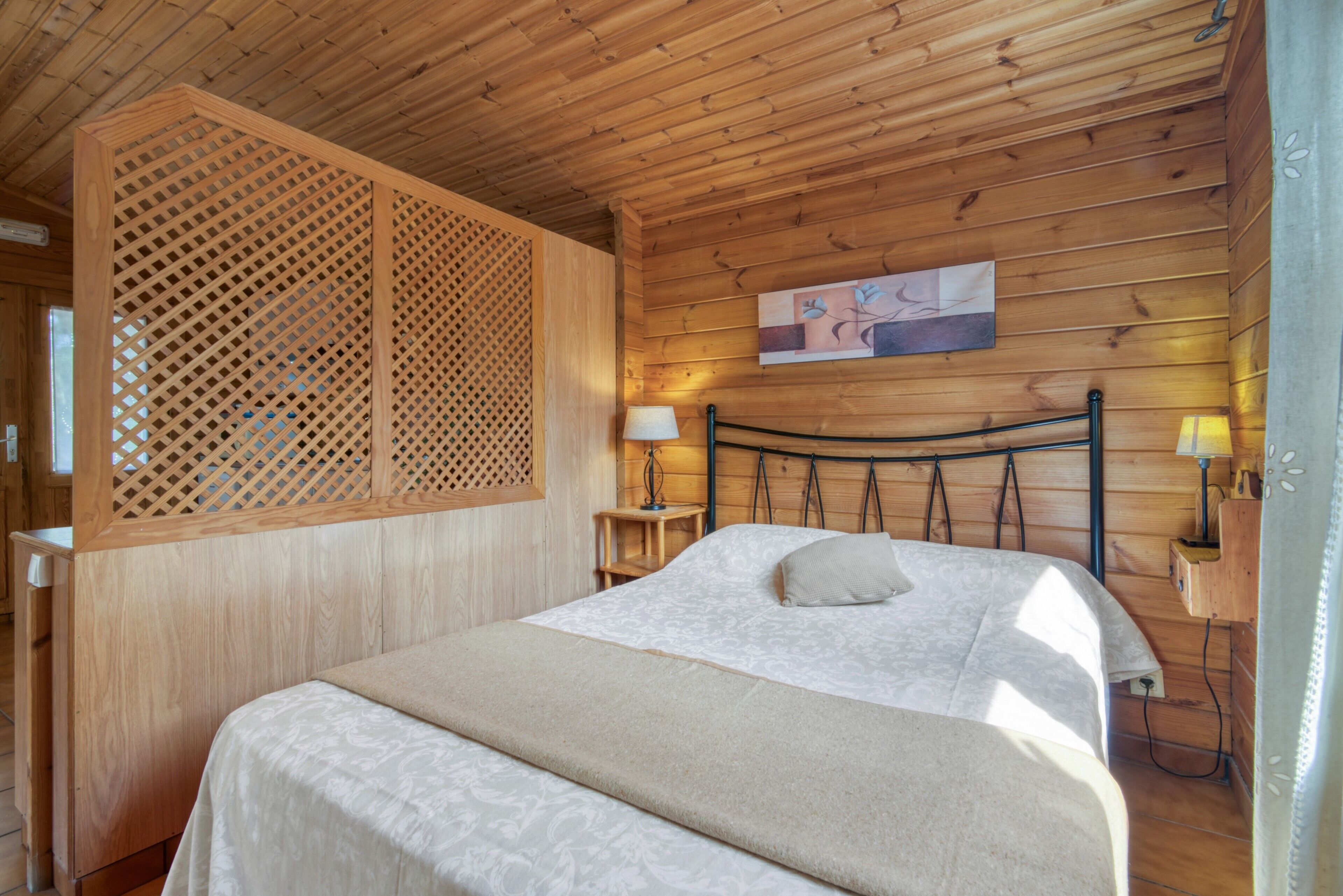A wooden cabin bedroom with a bed, a nightstand, a lamp, and a wooden partition.