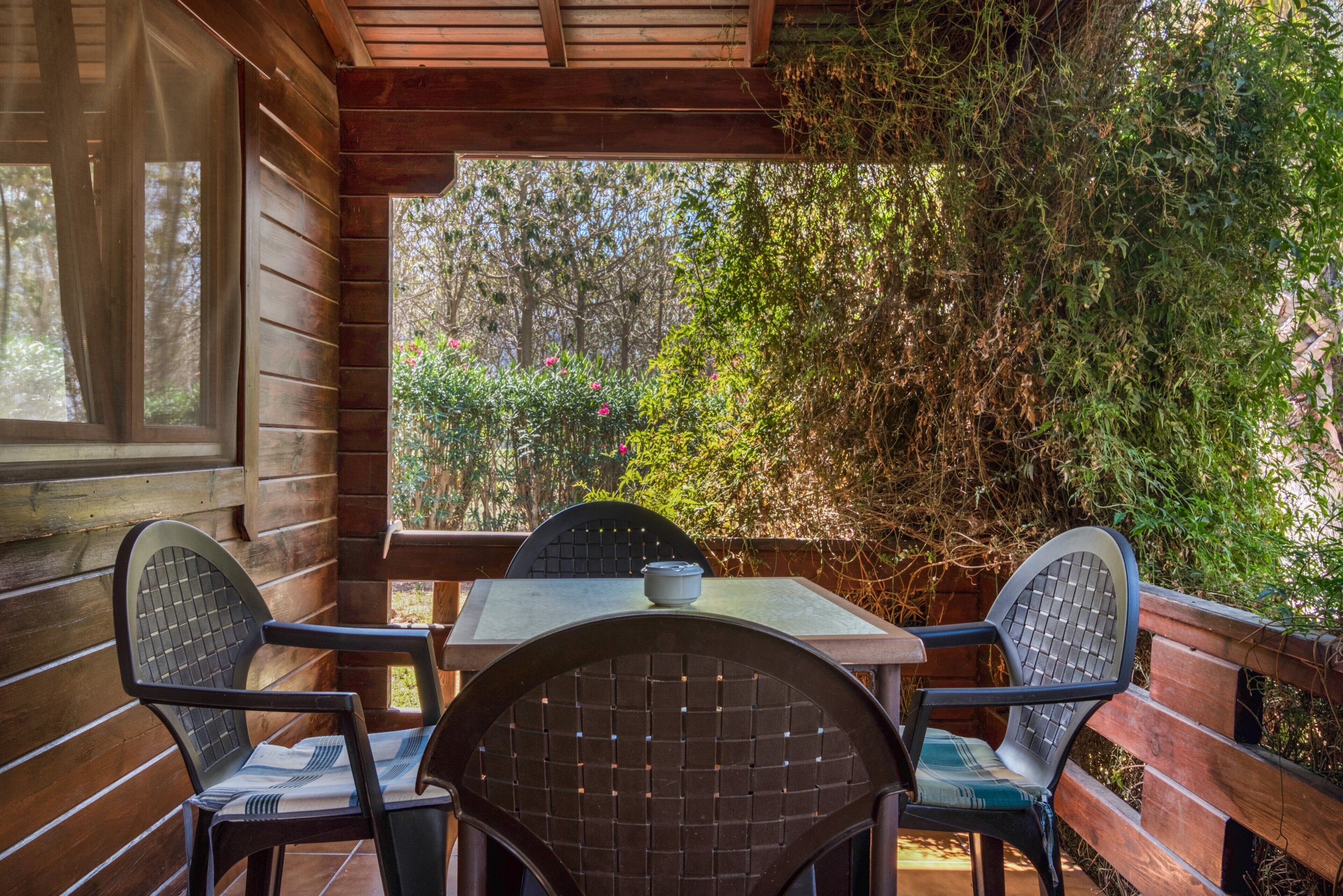 A wooden deck with a table and chairs, surrounded by dense foliage.