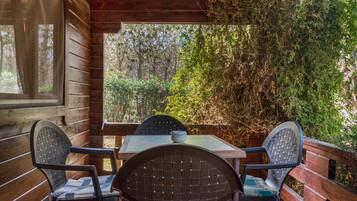 A wooden deck with a table and chairs, surrounded by dense foliage.