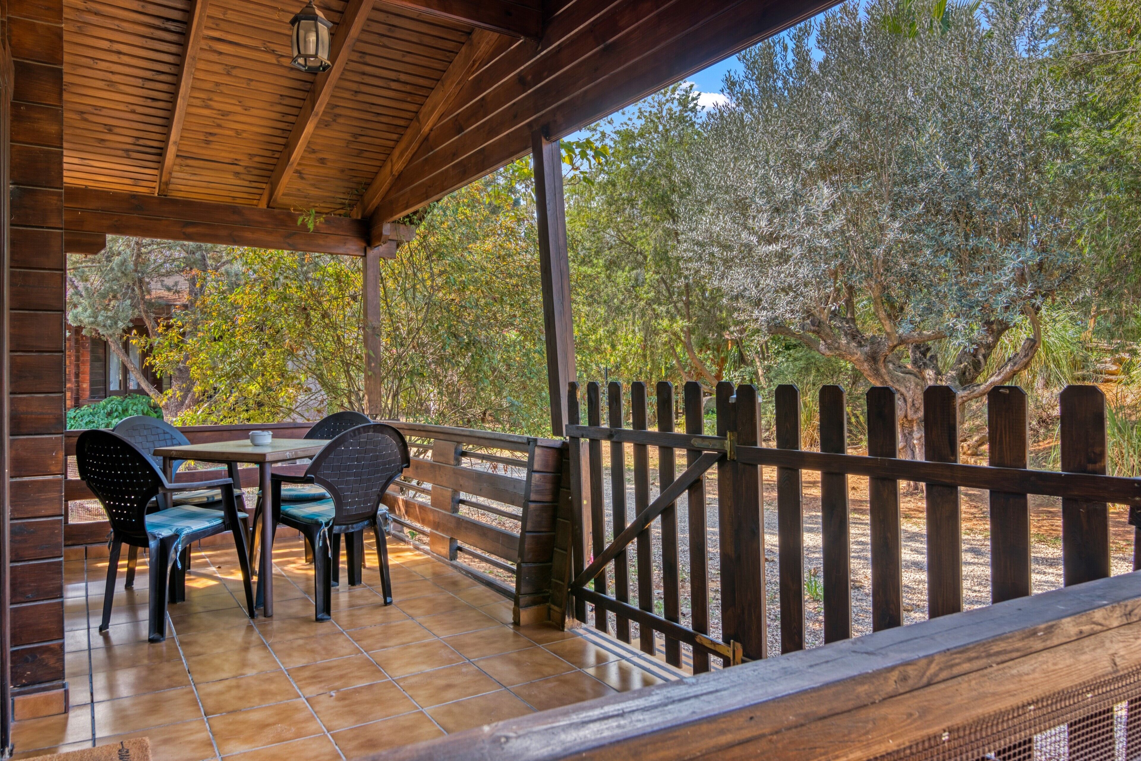 A covered patio with a wooden fence, a table with chairs, and a view of trees.