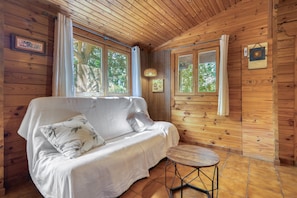 L’intérieur d’un chalet en bois, avec un canapé, une petite table et de grandes fenêtres.