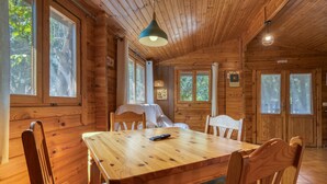 Interior de una cabaña de madera con una mesa de comedor, sillas y una lámpara colgante.