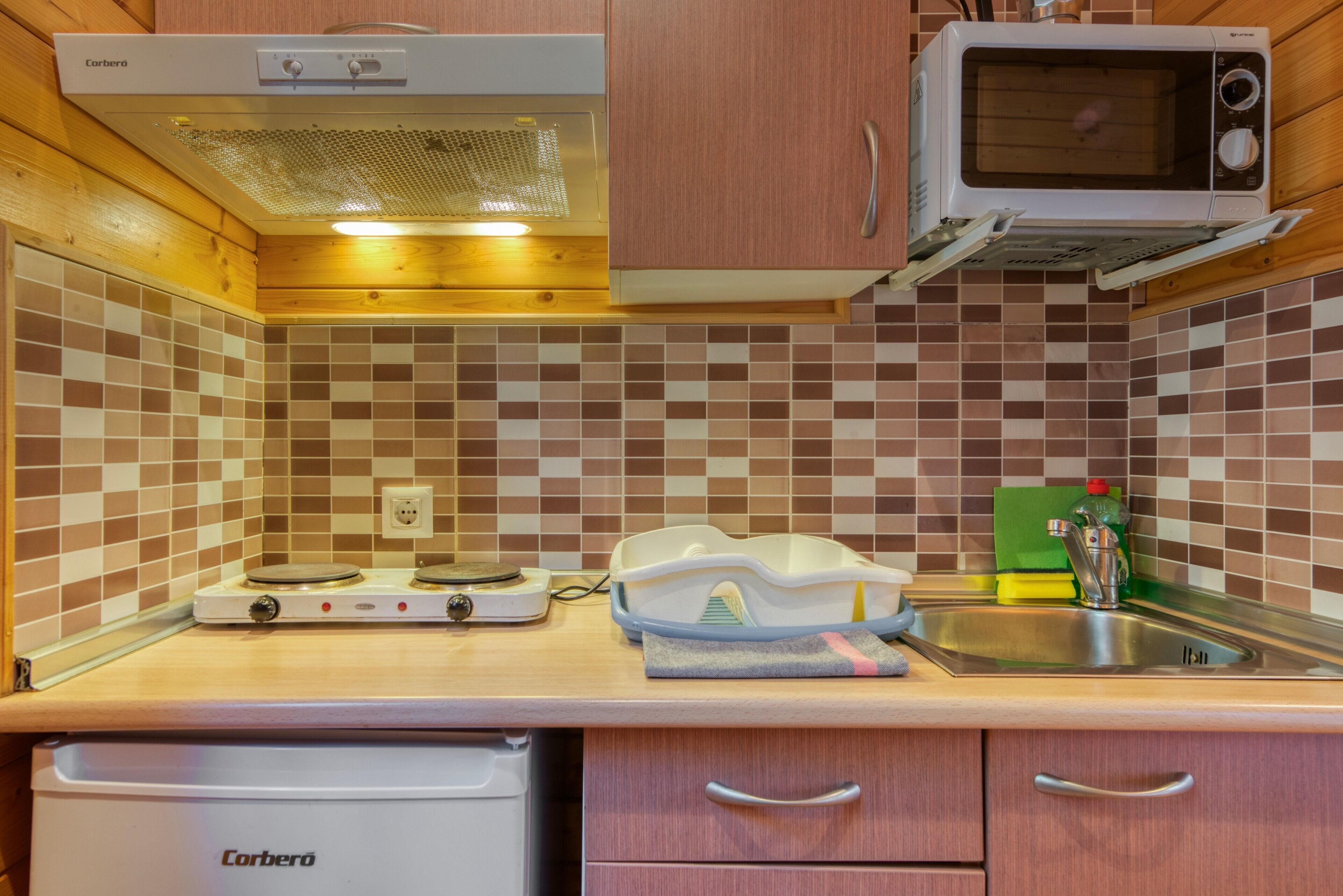 A compact kitchen with a Corbero stove, a microwave, and a sink.