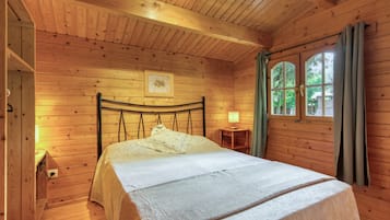 A wooden cabin bedroom with a bed, a nightstand, a window with curtains, and a framed picture on the wall.