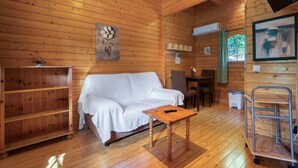 Interior de una cabaña de madera con un sofá blanco, una mesita, un televisor y una estantería.