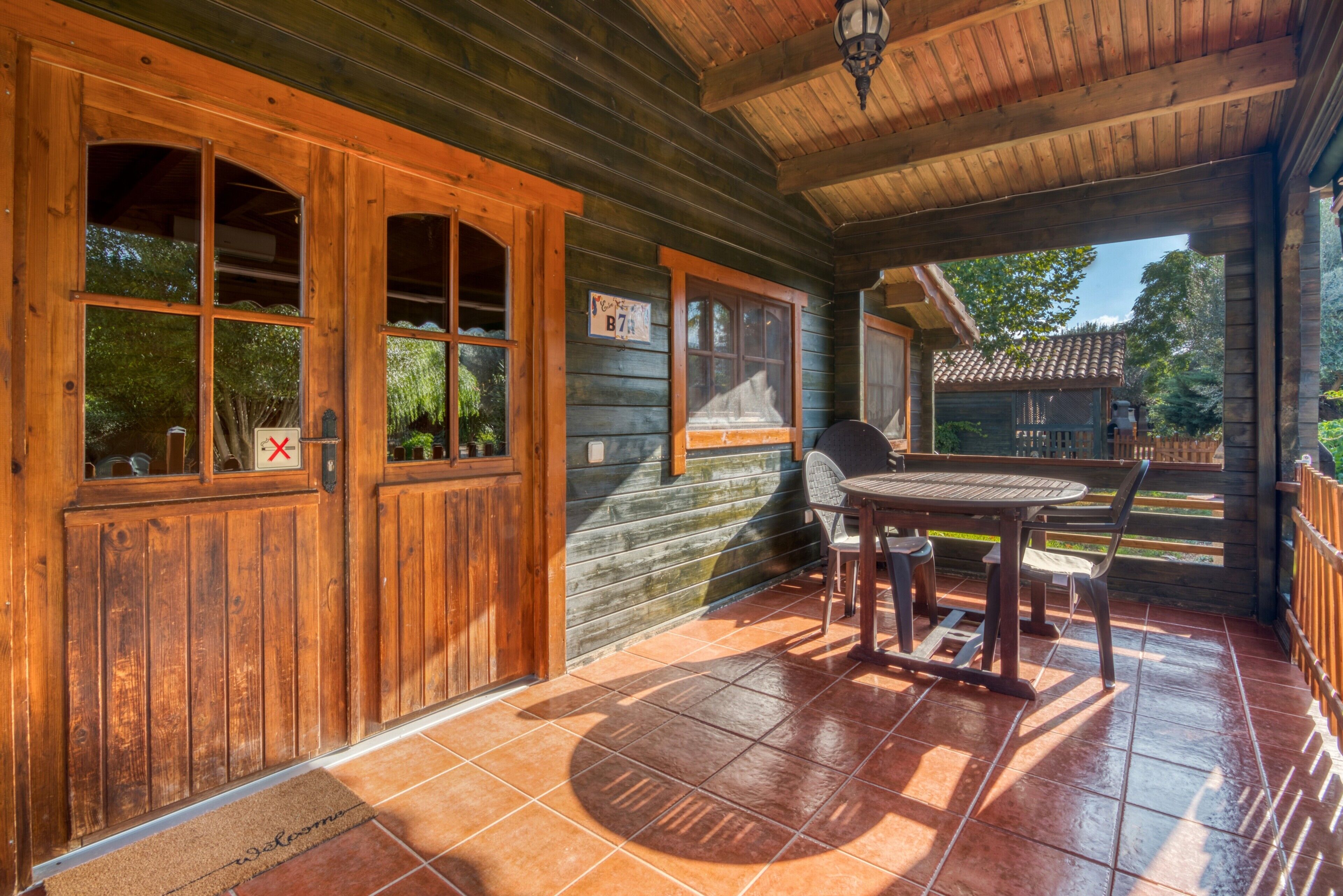 Eine Holzhütte mit Terrasse, inklusive Tisch und Stühlen, einer Holztür mit Fenstern und einem Schild mit der Nummer 87.