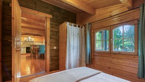 A wooden cabin interior with a bed, a shower area, and a view of the outdoors through a window.