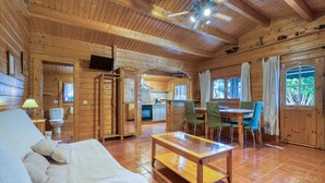 A wooden cabin interior with a sofa, a dining table with chairs, a television, and a ceiling fan.