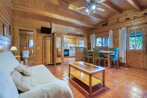 A wooden cabin interior with a sofa, a dining table with chairs, a television, and a ceiling fan.
