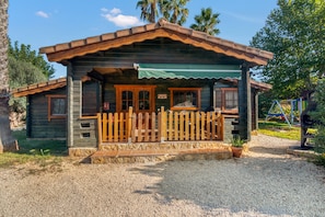 A rustic wooden cabin with a porch, a sign, and a gravel driveway.