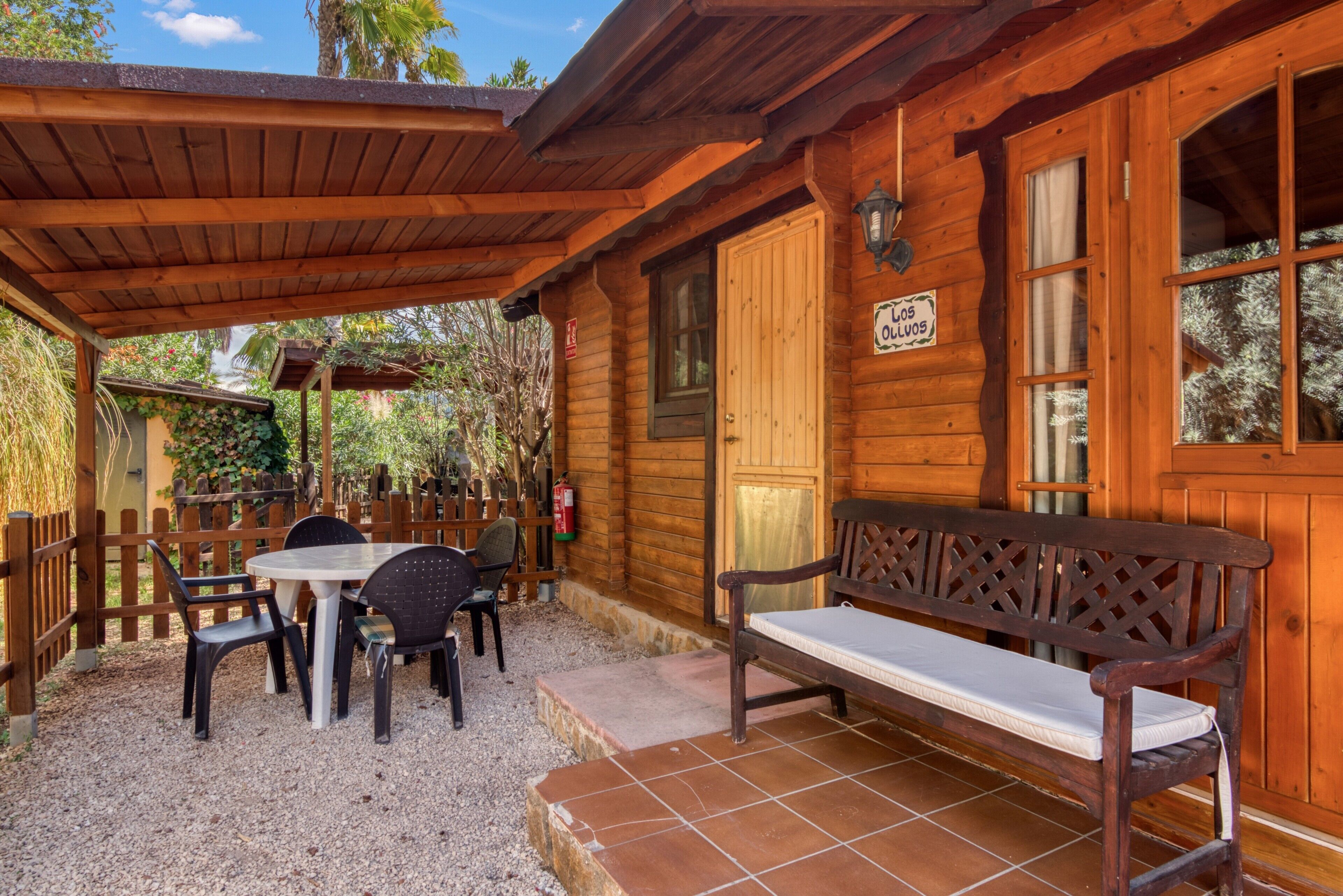 Una cabaña de madera con un porche cubierto, un banco y una mesa con sillas.