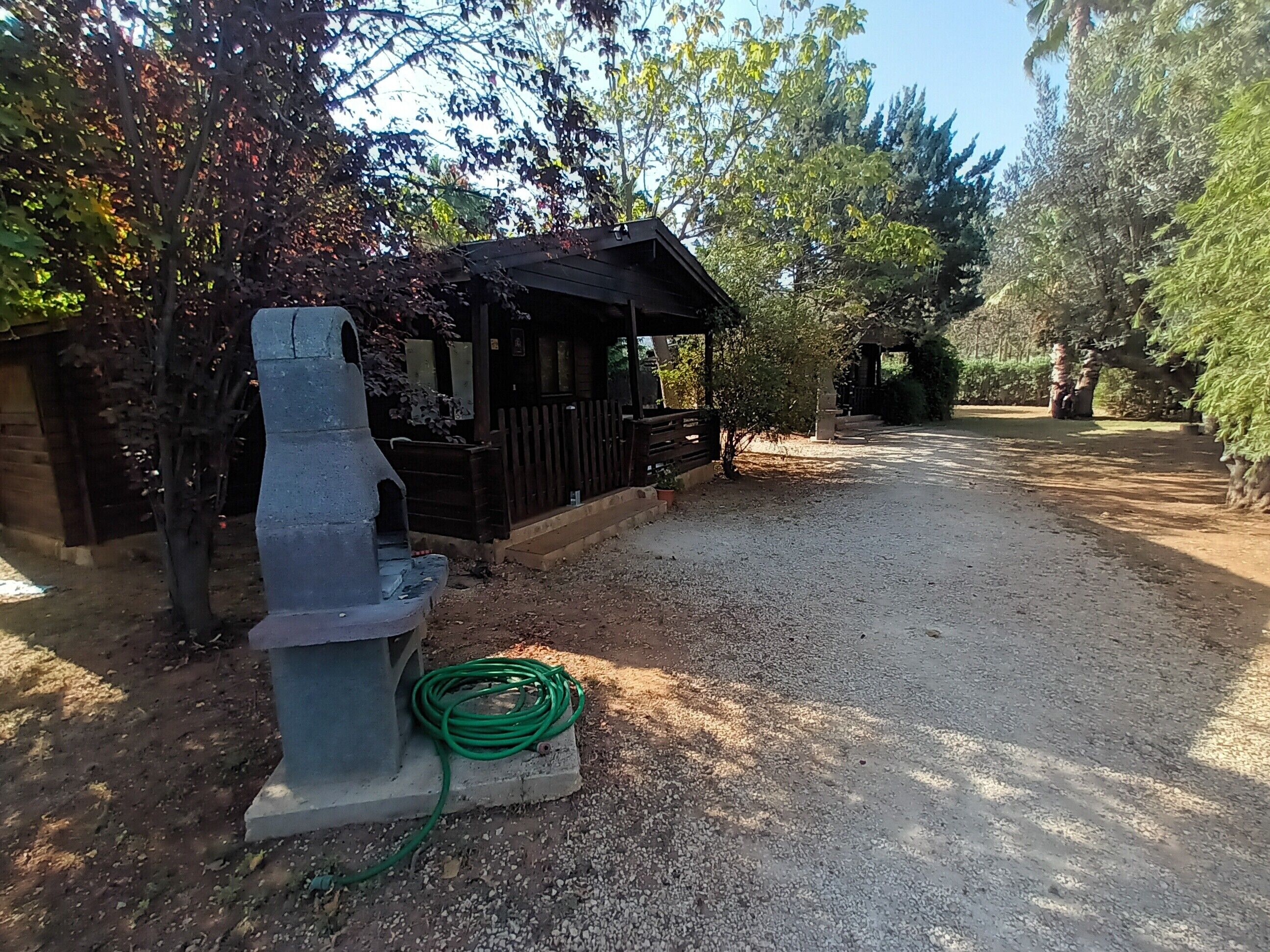 Una cabaña rústica con un camino de grava, rodeada de árboles y una valla de madera.