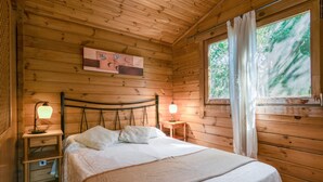 Une chambre à coucher dans un chalet en bois, avec un lit, des lampes de chevet, une table de chevet et une fenêtre avec des rideaux.