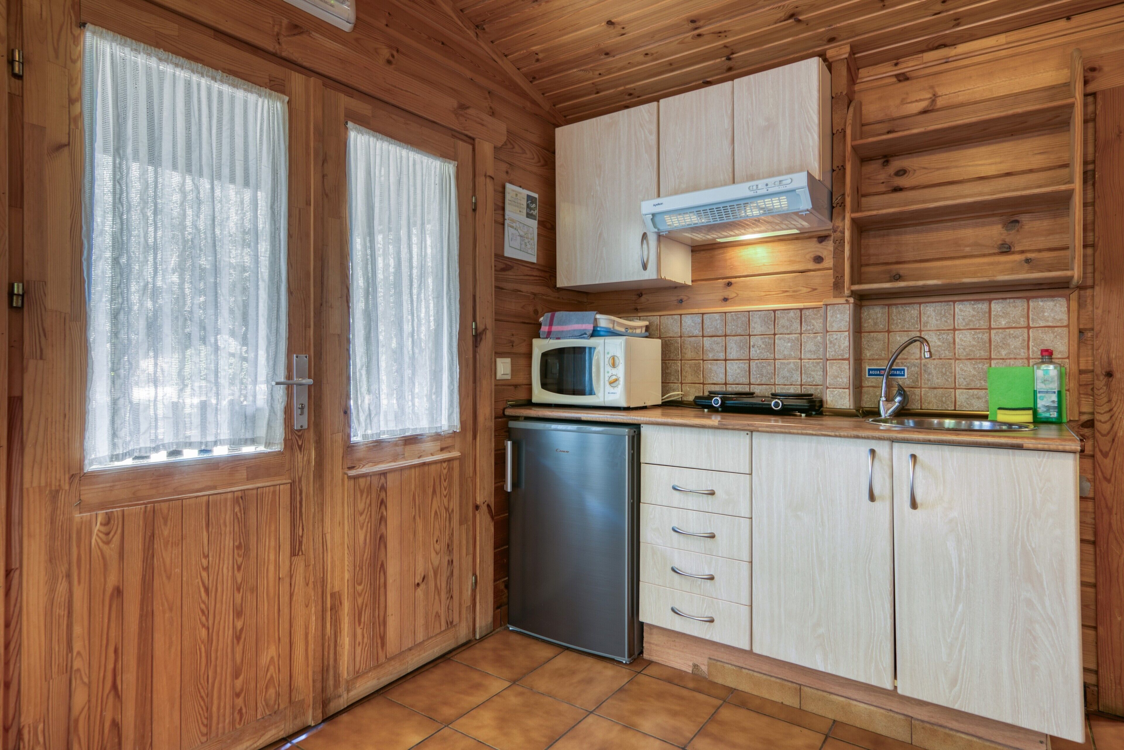 A compact kitchen with wooden cabinets, a microwave, a sink, and a small refrigerator.