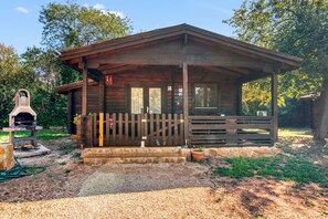 Une cabane en bois avec une véranda, une cheminée en briques et une clôture en bois.