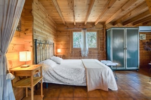 A wooden cabin bedroom with a bed, a nightstand, a lamp, a window, and a wardrobe.