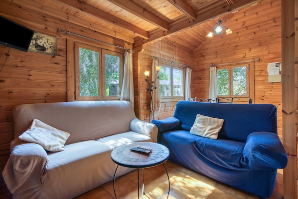 A wooden cabin interior with two sofas, a small table, and a ceiling fan.