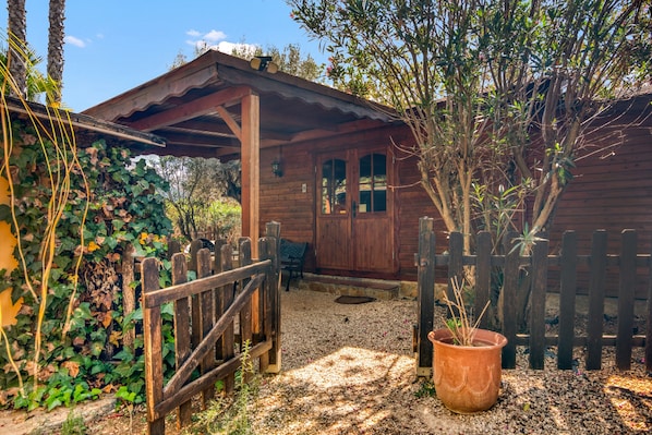 A wooden cabin with a porch, a gravel path, and a wooden fence.