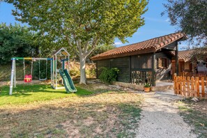 Une cabane en bois avec un toit en tuiles, une balançoire et un chemin de gravier.