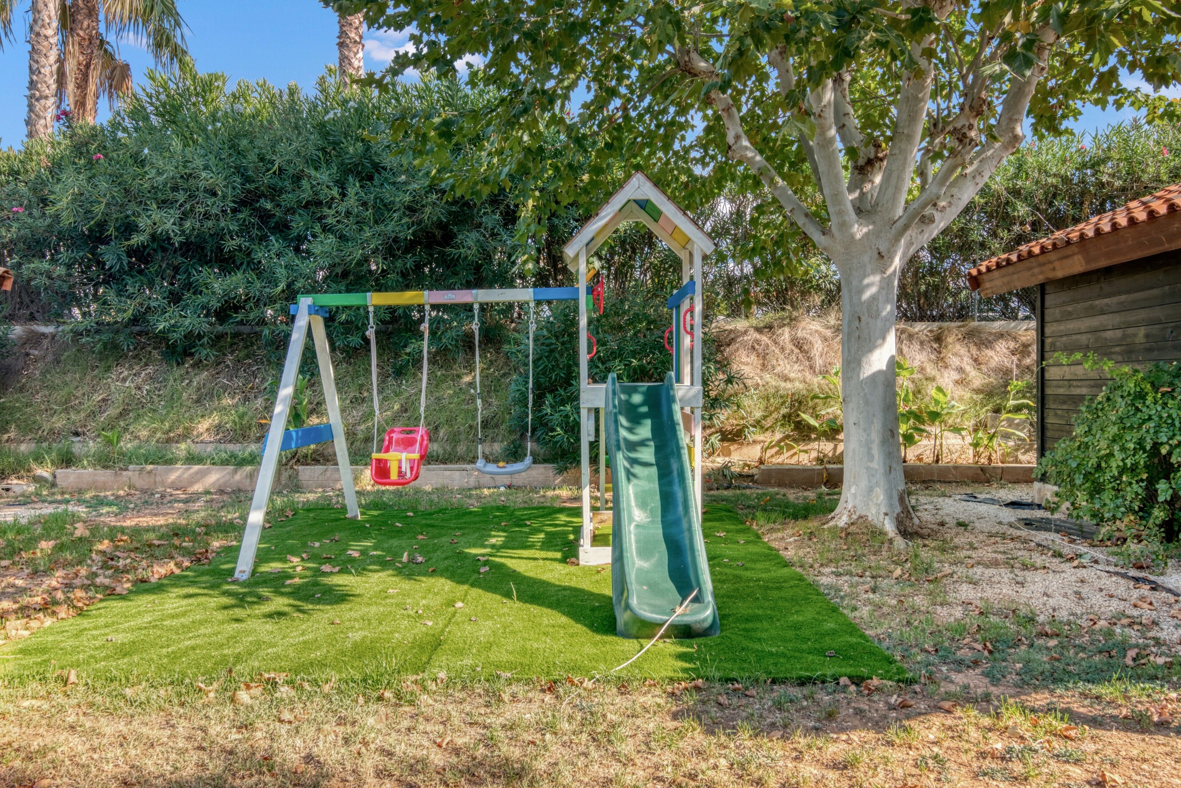 Ein Spielplatz mit Schaukel und Rutsche, umgeben von Gras und Bäumen.