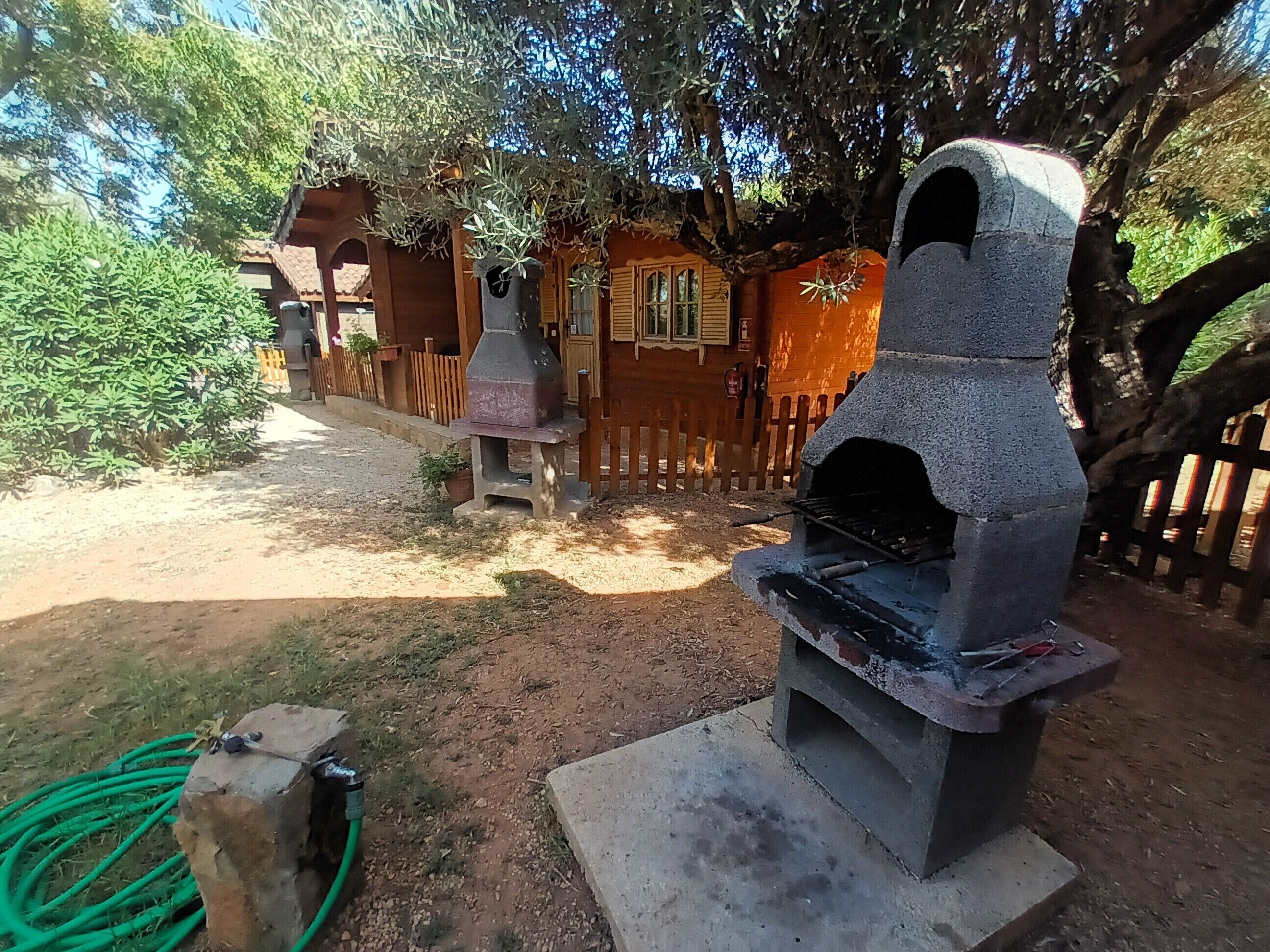 An outdoor area with a stone oven, a wooden fence, and a building with a window.