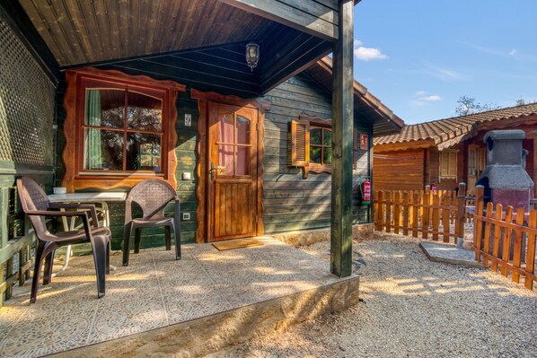 Une cabane en bois avec un porche, une table et des chaises, et un chemin de gravier.