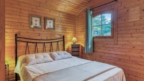 A wooden cabin bedroom with a bed, a window, and framed pictures on the wall.