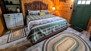 Acogedora habitación tipo cabaña de madera con una cama, una mesita de noche, una lámpara, una puerta verde y un armario con espejo.